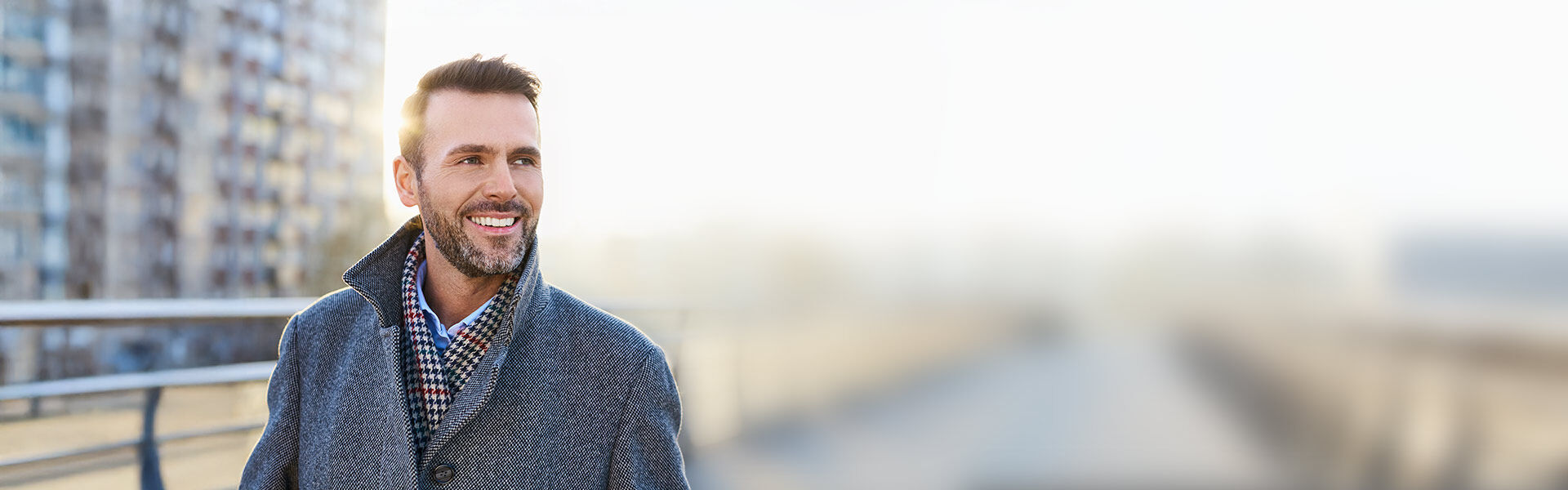 Mann im grauen Mantel steht draußen vor einem Gebäude.