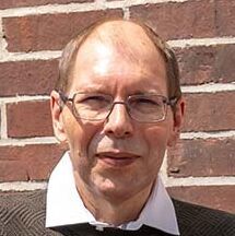 Der erfolgreiche Umschüler André Pardun steht mit verschränkten Armen vor einer geziegelten Hauswand.