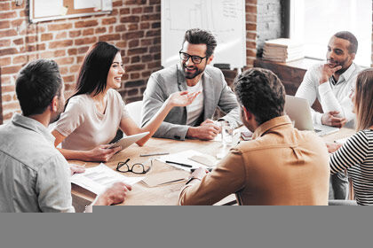 eine Gruppe von Menschen, die um einen Tisch sitzen und zwei Männer die Hände schütteln