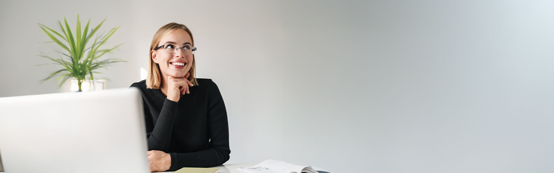 Coachings: Junge Frau sitzt vor einem Laptop und schaut nach ihrem Einzelcoaching glücklich lächelnd zur Seite.