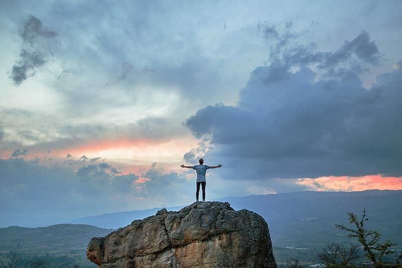 Ein Mann steht auf dem Berggipfel und streckt die Arme aus.